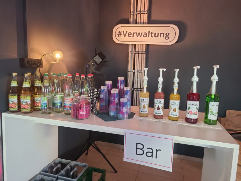 Bar mit verschiedenen Säften, Wassersorten und Sirups. Darüber ein Schild: #Verwaltung