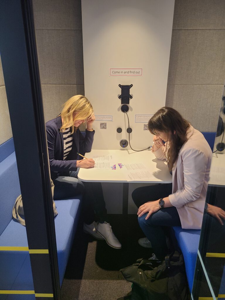 zwei Personen sitzen in einer schallgeschützten Kabine und füllen einen Test aus