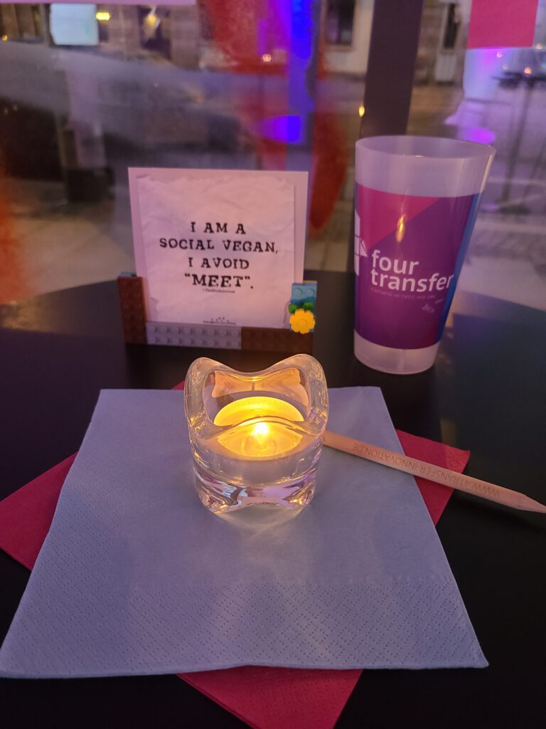 Stimmungsbild von der Deko der Stehtisch: bunte Servietten, Teelicht. Getränkebecher, Bleistift und ein Legoaufsteller mit der Aufschrift: I am a social vegan. I avoid 