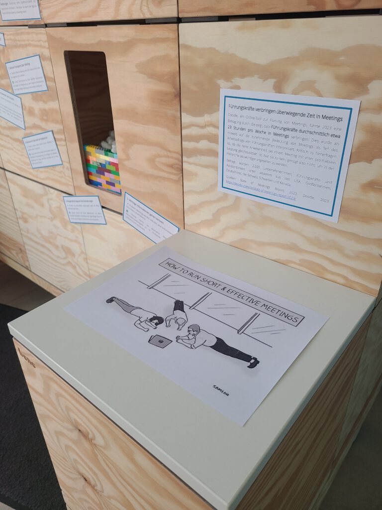 Detail des Ausstellungsregals. Abgebildet ist ein Meme auf dem drei Personen eine Sportübung machen; Überschrift 